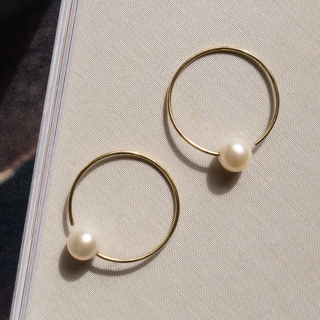 Ein Paar filigrane goldene Ohrringe mit schlichten, kreisförmigen Ringen und edlen Perlen, die minimalistische Eleganz und zeitlose Schönheit ausstrahlen.