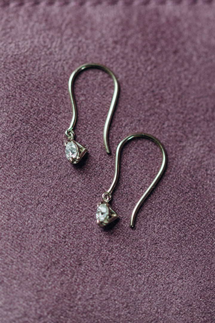 Elegante Emilia Diamantohrhänger mit zarten Haken und beweglichen Diamanten, fotografiert auf violettem Samt.