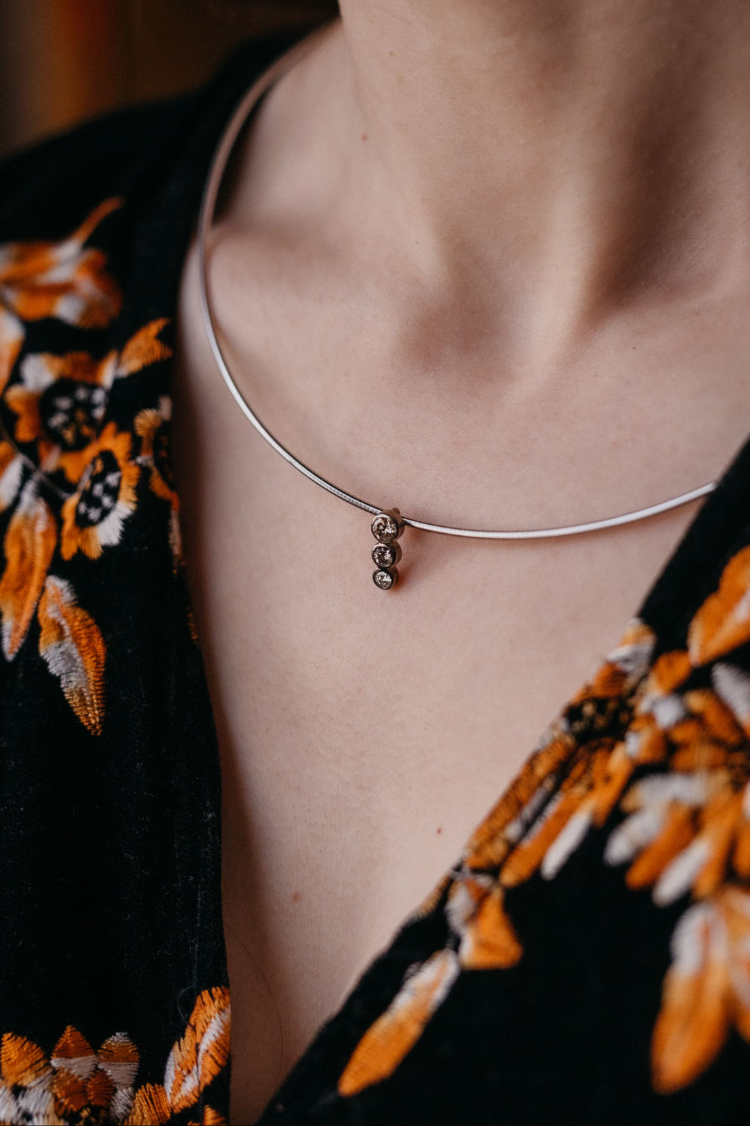 Nahaufnahme einer Frau, die die Estelle Halskette aus Weißgold mit drei funkelnden Diamanten trägt. Der elegante Anhänger liegt zart am Hals und hebt das Dekolleté dezent hervor.