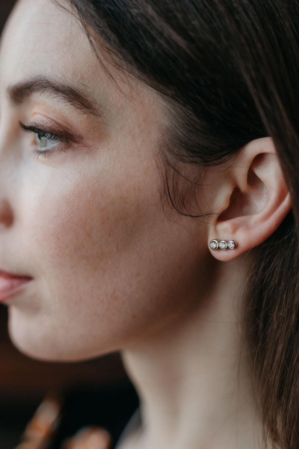 Weißgold-Ohrringe „Estelle“ mit drei Diamanten, elegant am Ohr eines Models getragen – seitliches Portrait mit Fokus auf dem Schmuck.