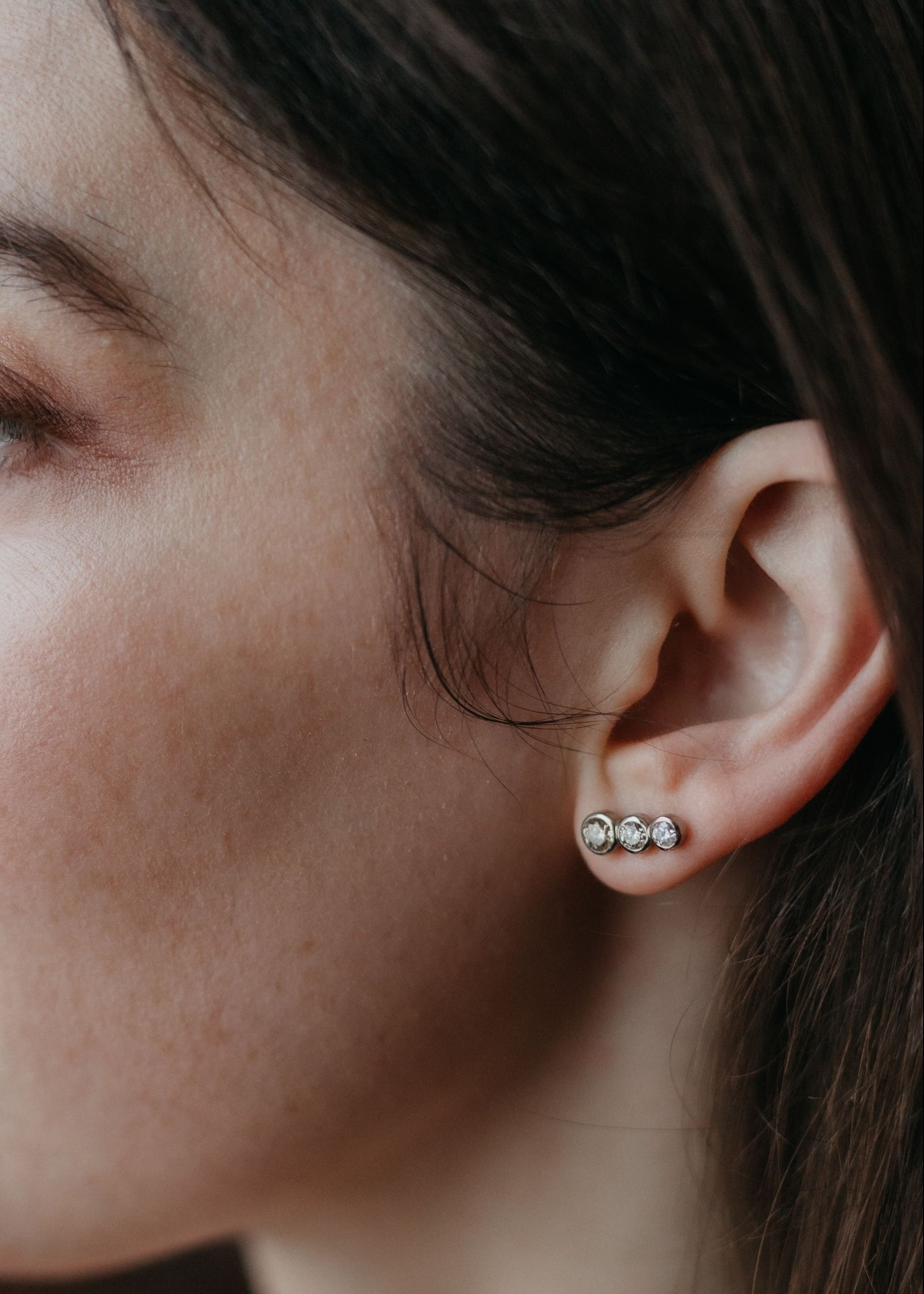 Weißgold-Ohrringe „Estelle“ mit drei Diamanten, elegant am Ohr eines Models getragen – seitliches Portrait mit Fokus auf dem Schmuck.