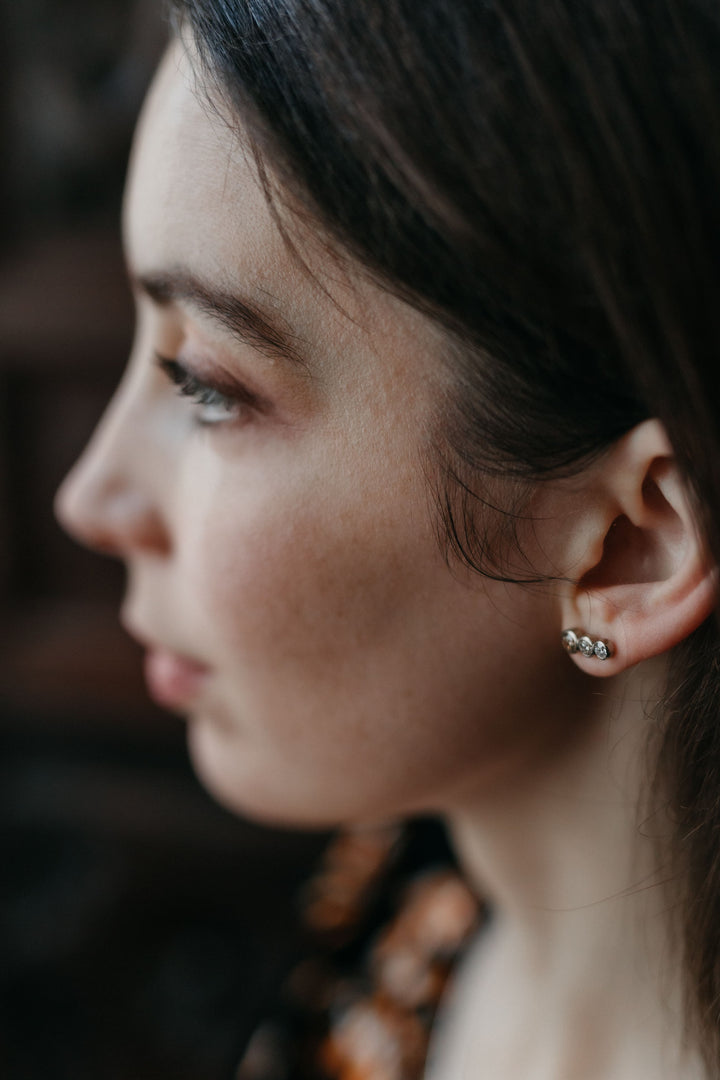 Feine „Estelle“ Ohrstecker aus Weißgold mit drei funkelnden Diamanten, dezent am Ohr eines Models – seitliche, leicht unscharfe Aufnahme