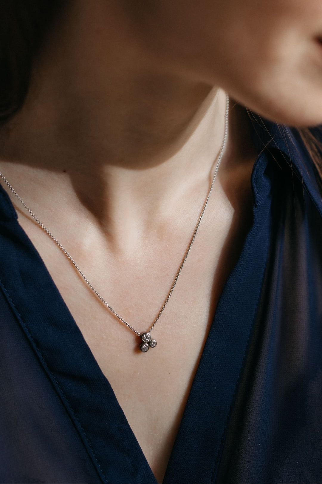 Nahaufnahme des Gloria Anhängers in Weißgold an einer feinen Kette, getragen von einem Modell in dunkelblauer Bluse.