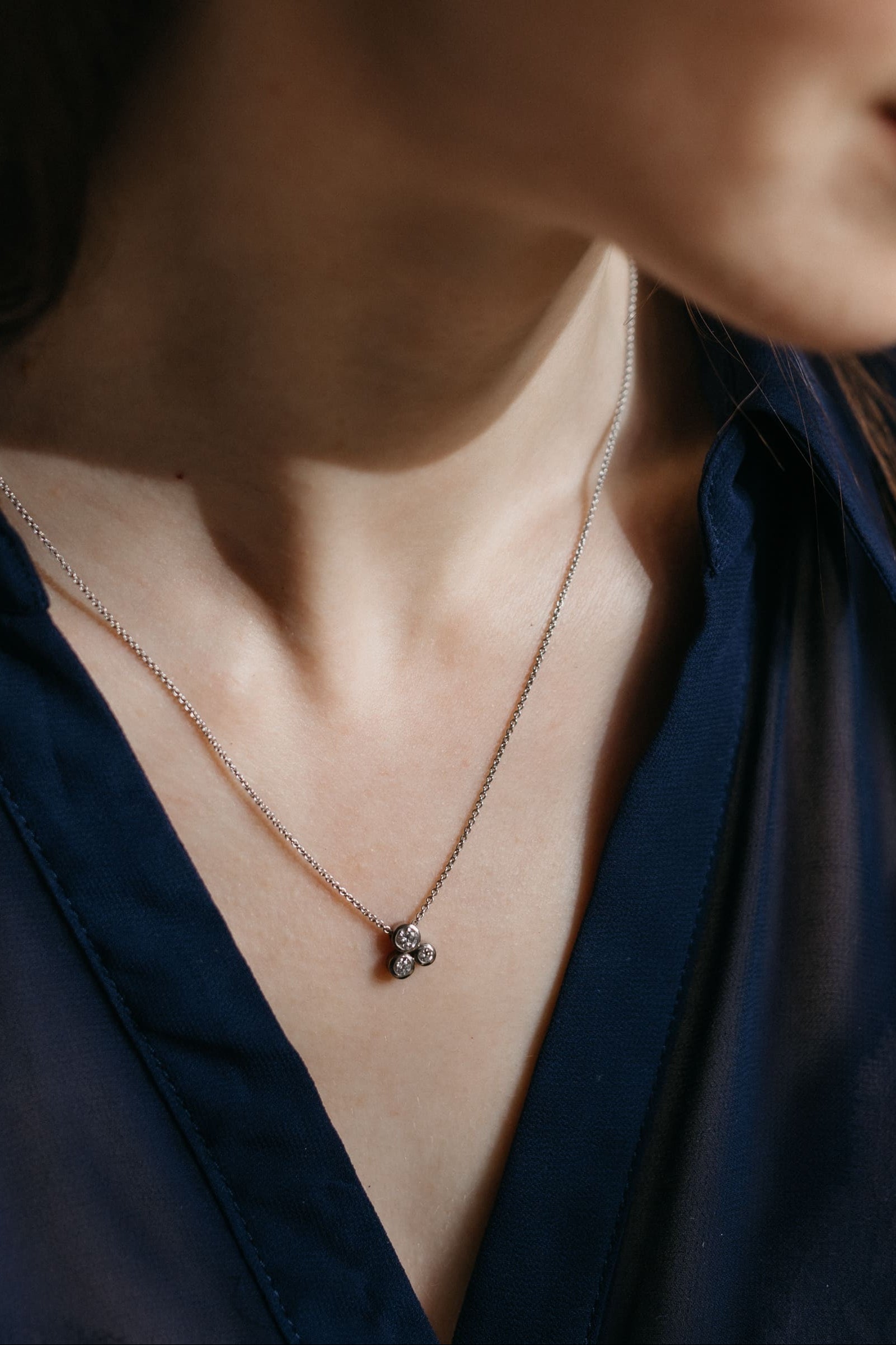 Nahaufnahme des Gloria Anhängers in Weißgold an einer feinen Kette, getragen von einem Modell in dunkelblauer Bluse.