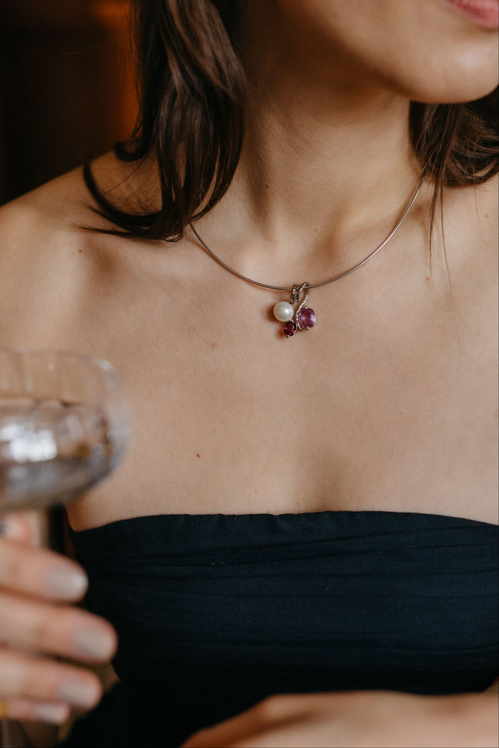 Frau trägt den Mon Amour Ring und passenden Anhänger aus Weißgold mit Perle und violetten Edelsteinen im warmen Fensterlicht.