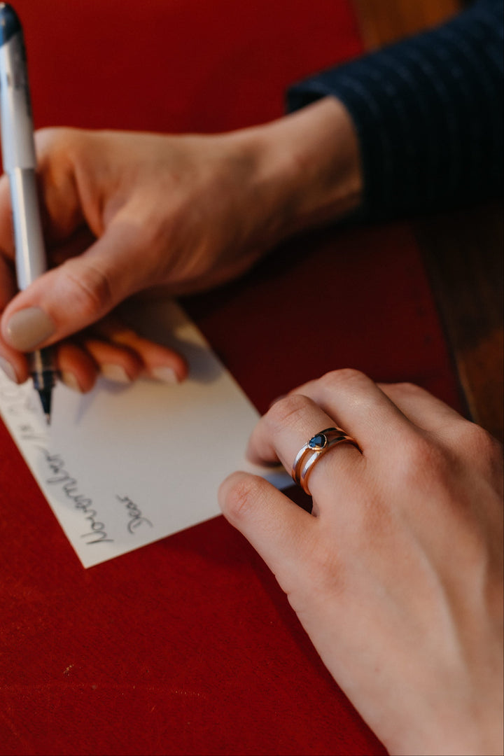 Nahaufnahme der Hand mit dem Mon Cœur Ring in Gelbgold und herzförmigem Edelstein beim Schreiben einer Karte.