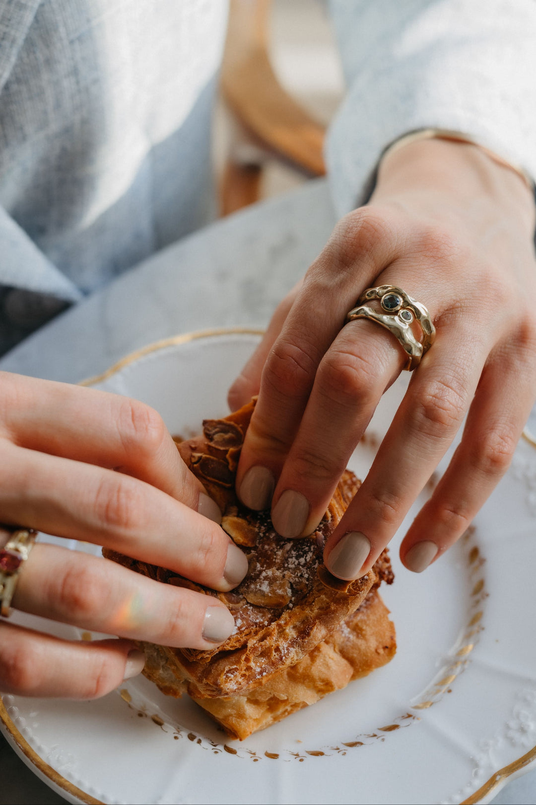 Mystery Ring aus Gold mit blauem Edelstein, am Finger getragen beim Genießen eines Gebäcks.