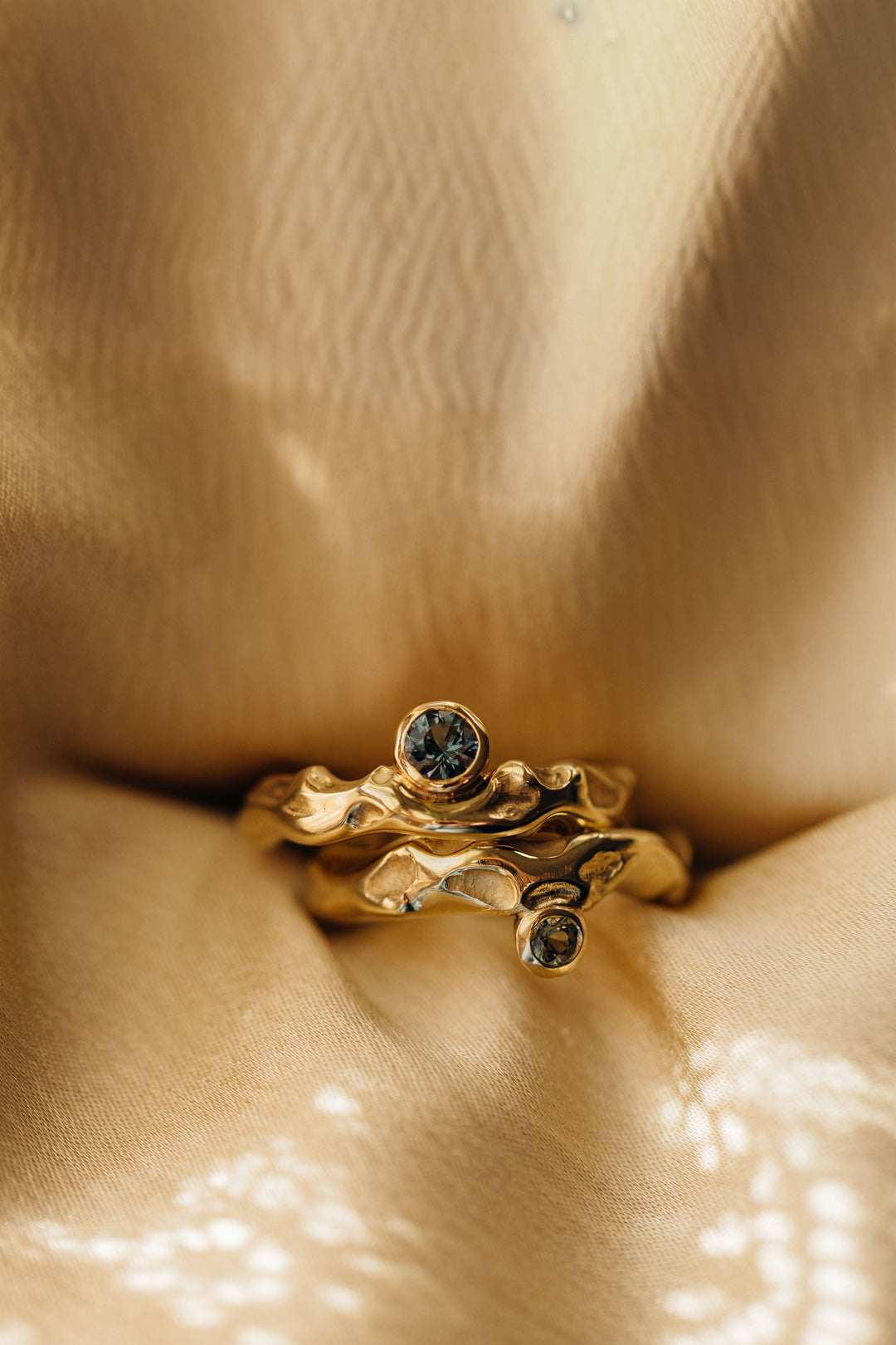 Goldener Mystery Single Ring mit organischer Oberfläche und Turmalin, stimmungsvoll im warmen Licht auf Stoff in Szene gesetzt.