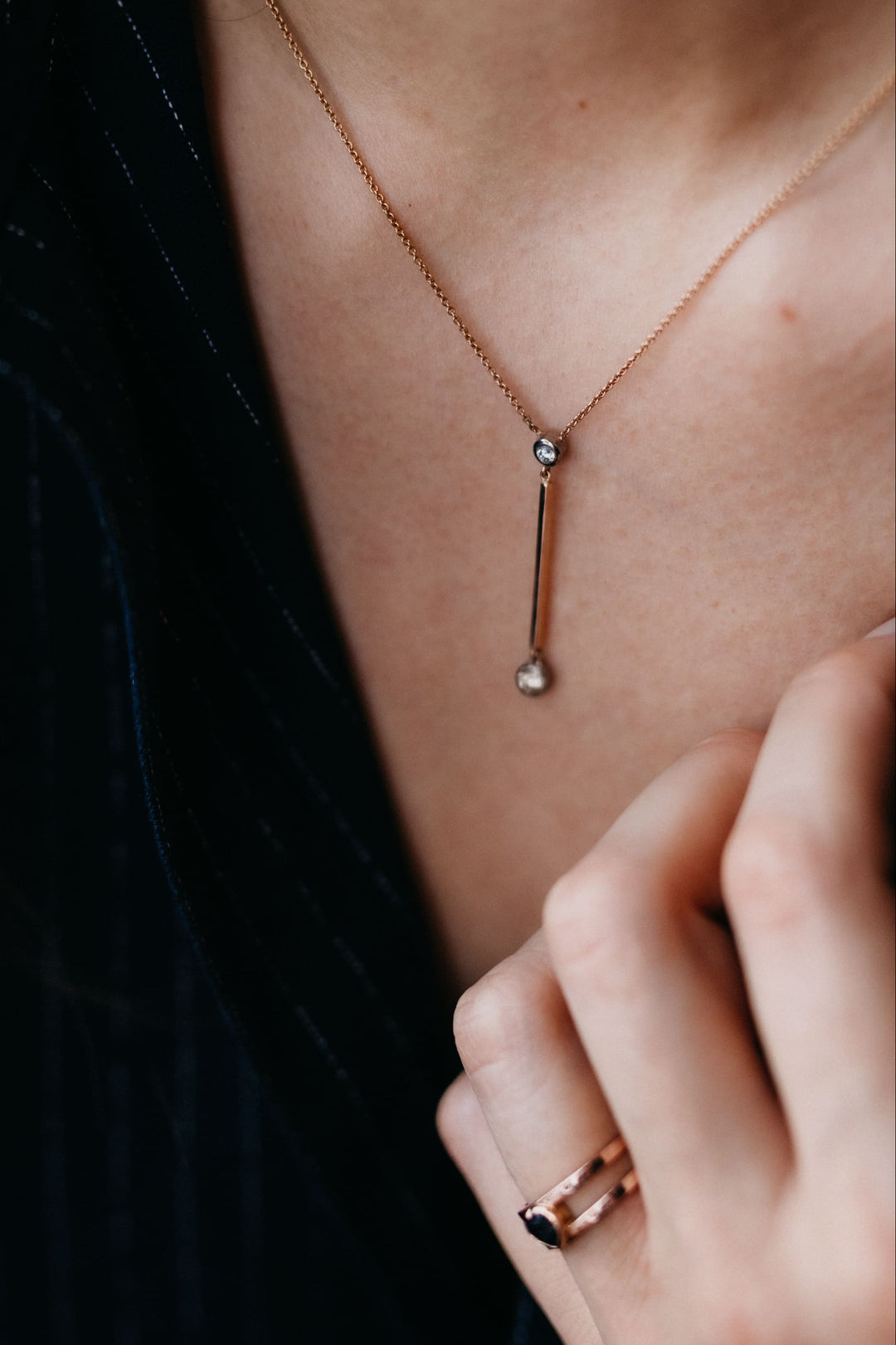 Valentina Collier in Roségold mit langem Stabanhänger und zwei brillantgefassten Diamanten, präsentiert auf samtigem Hintergrund von leicht vorlehnender Person