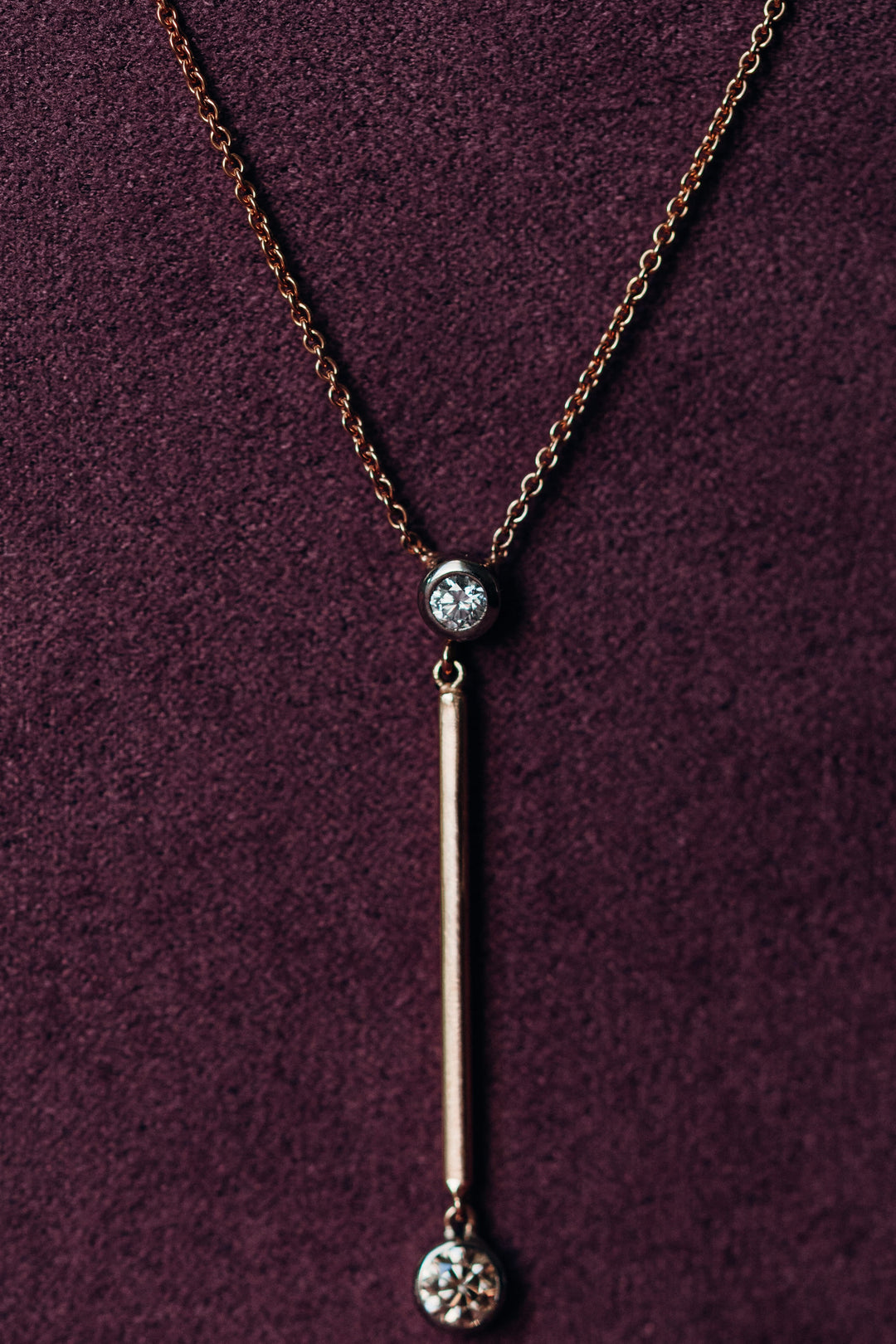 Valentina Collier in Roségold mit langem Stabanhänger und zwei brillantgefassten Diamanten, präsentiert auf samtigem Hintergrund.