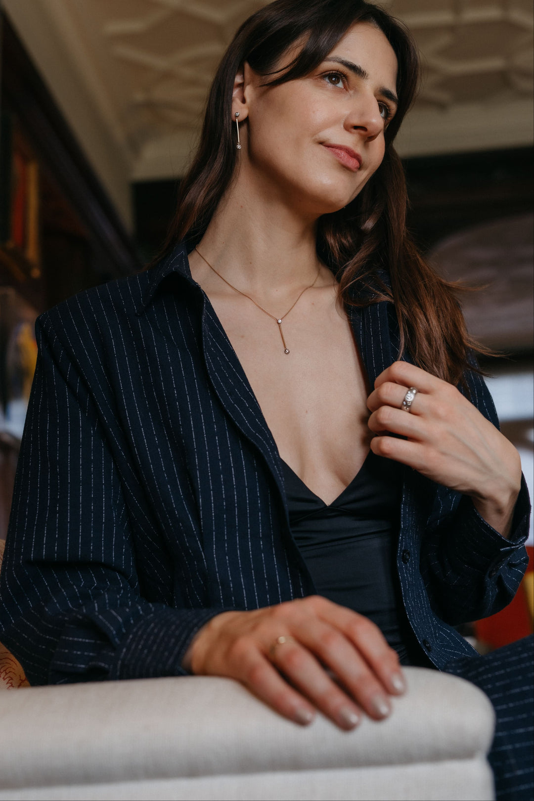 Person, die Valentina-Halskette und Valentina-Ohrringe trägt, sitzend in einem kunstvollen Wohnzimmer.