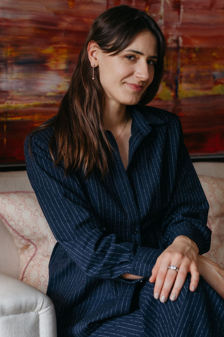 Portraitaufnahme einer Person, die Valentina-Halskette, Ohrringe und Ring trägt und auf einem Sofa sitzt und in die Kamera guckt.