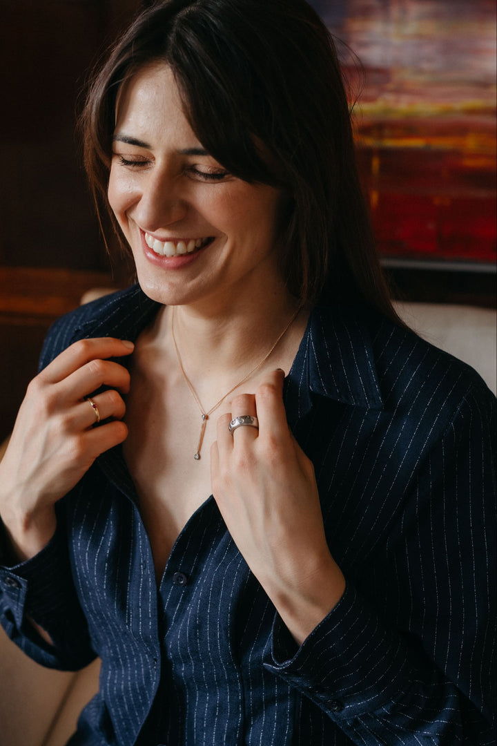 Portraitaufnahme einer Person, die Valentina-Halskette, Ohrringe und Ring trägt und auf einem Sofa sitzt.